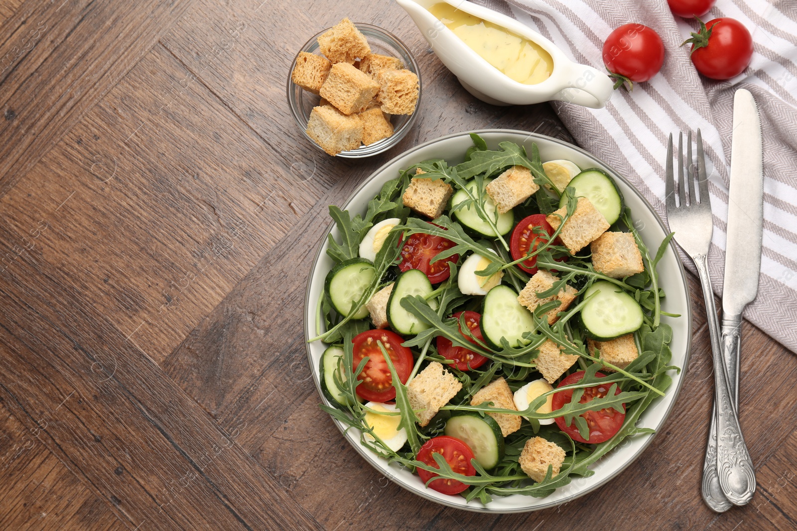 Photo of Tasty salad with croutons, cucumbers, tomatoes and arugula on wooden table, flat lay. Space for text