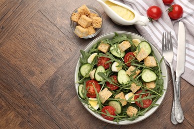 Photo of Tasty salad with croutons, cucumbers, tomatoes and arugula on wooden table, flat lay. Space for text