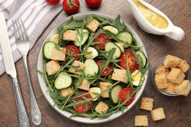 Photo of Tasty salad with croutons, cucumbers, tomatoes and arugula on wooden table, flat lay