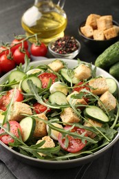 Photo of Tasty salad with croutons, cucumbers, tomatoes and arugula on black table, closeup