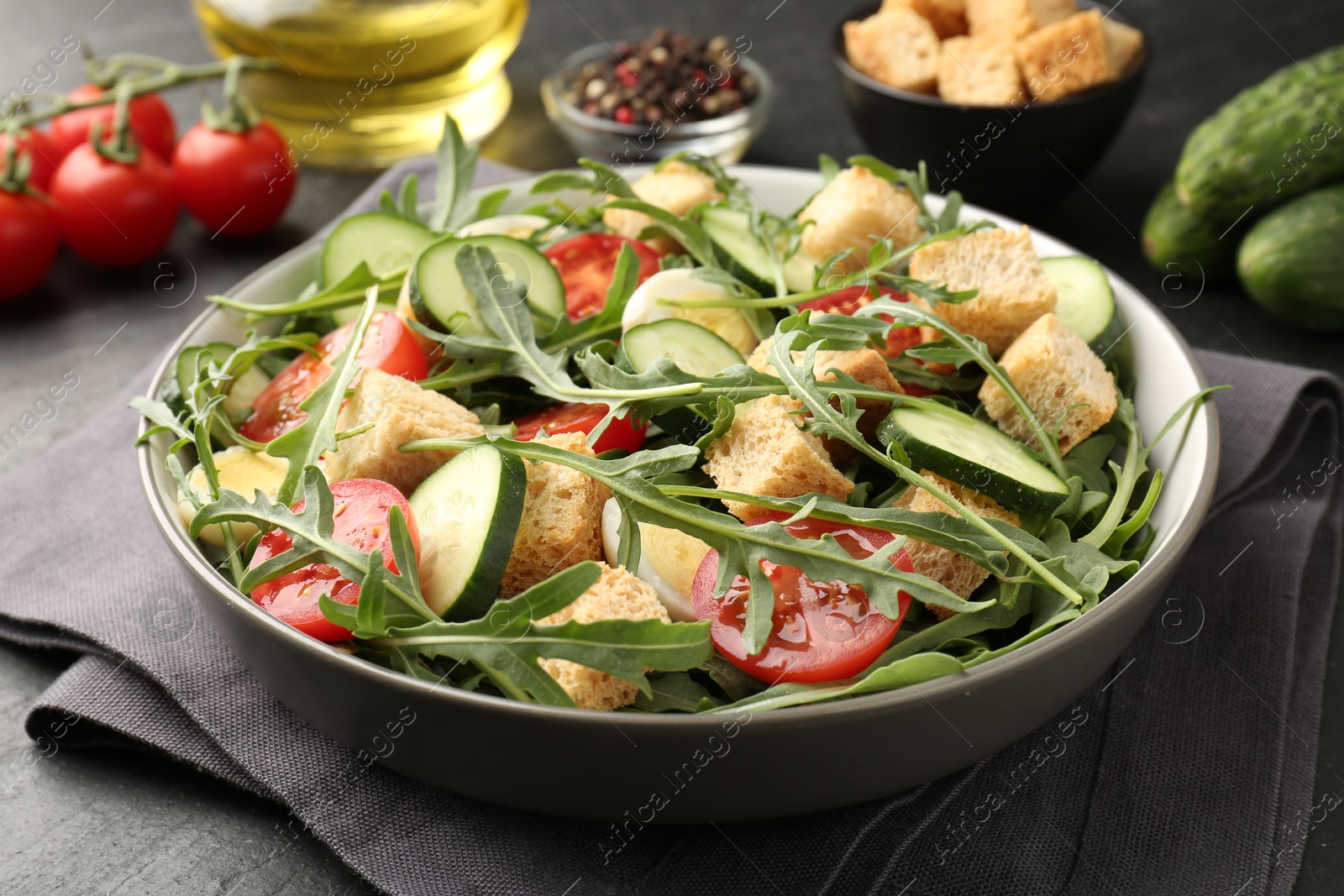 Photo of Tasty salad with croutons, cucumbers, tomatoes and arugula on black table, closeup
