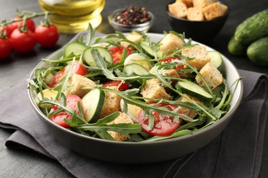 Photo of Tasty salad with croutons, cucumbers, tomatoes and arugula on black table, closeup