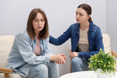 Photo of Woman apologizing to her offended friend on armchair near grey wall at home