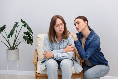 Photo of Woman apologizing to her offended friend on armchair near grey wall at home