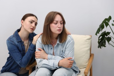 Photo of Woman apologizing to her offended friend on armchair near grey wall at home