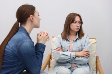 Photo of Woman apologizing to her offended friend on armchair near grey wall at home