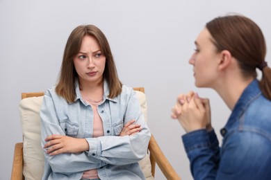 Photo of Woman apologizing to her offended friend on armchair near grey wall at home