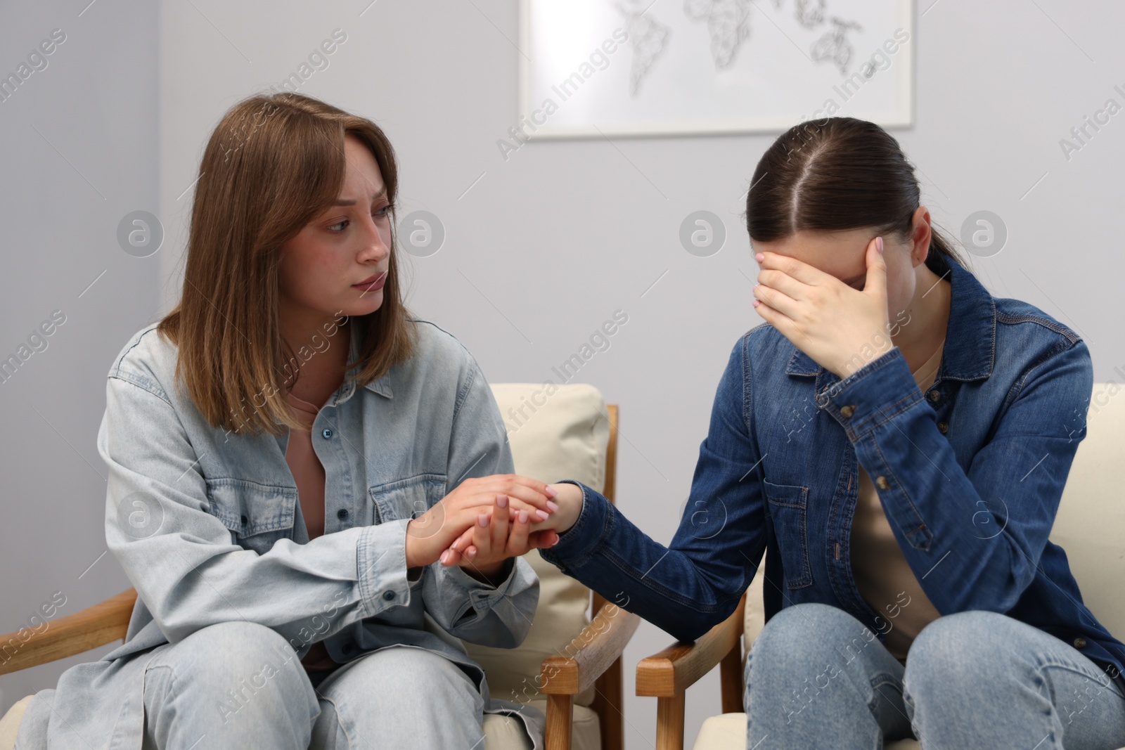 Photo of Woman apologizing to her offended friend on armchair near grey wall at home