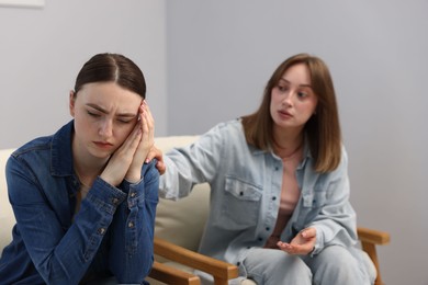 Photo of Woman apologizing to her offended friend on armchair near grey wall at home, selective focus
