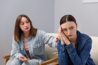 Photo of Woman apologizing to her offended friend on armchair near grey wall at home, selective focus