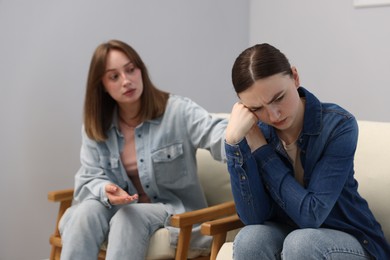Photo of Woman apologizing to her offended friend on armchair near grey wall at home, selective focus