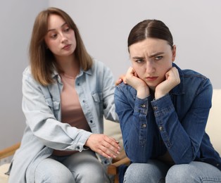 Photo of Woman apologizing to her offended friend on armchair near grey wall at home