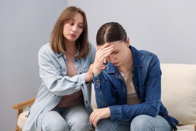 Photo of Woman apologizing to her offended friend on armchair near grey wall at home