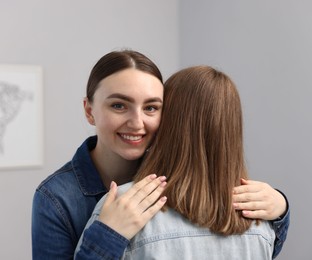Photo of Happy friends hugging after apology near grey wall at home