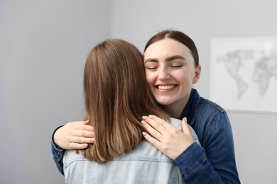 Photo of Happy friends hugging after apology near grey wall at home