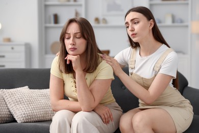 Photo of Woman apologizing to her offended friend on sofa at home