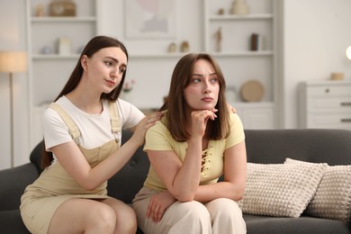 Photo of Woman apologizing to her offended friend on sofa at home