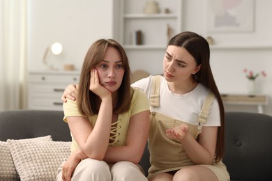 Photo of Woman apologizing to her offended friend on sofa at home