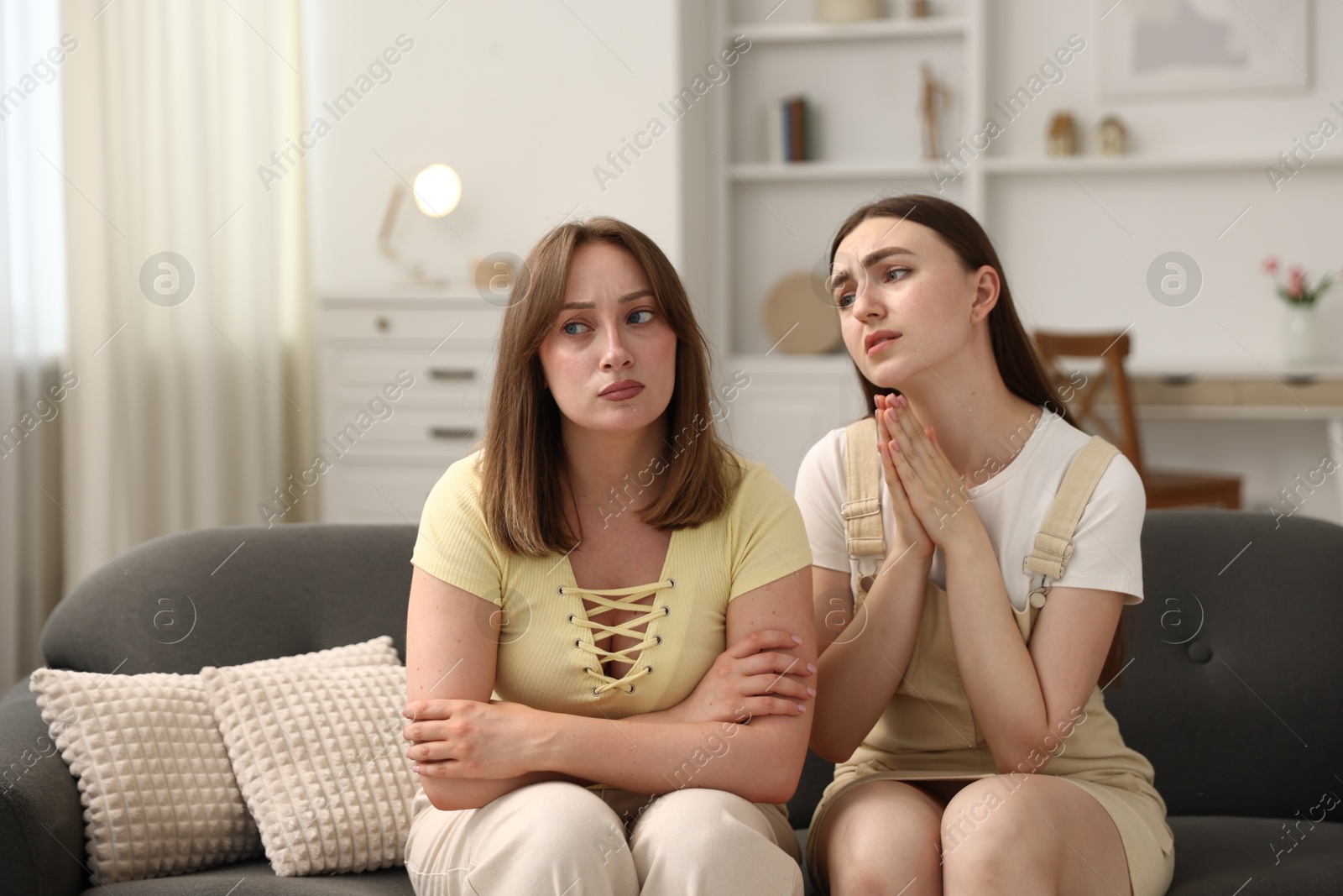Photo of Woman apologizing to her offended friend on sofa at home