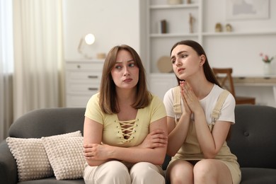 Photo of Woman apologizing to her offended friend on sofa at home