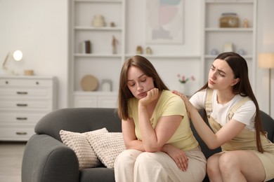 Photo of Woman apologizing to her offended friend on sofa at home