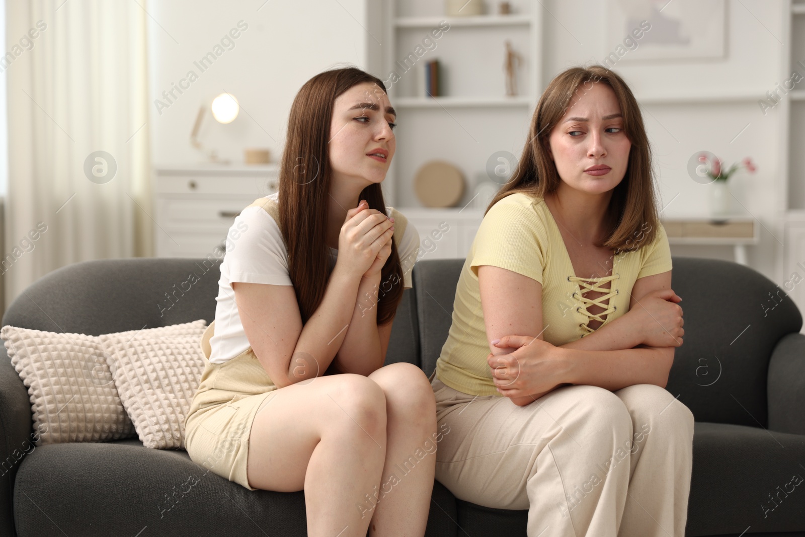 Woman apologizing to her offended friend on sofa at home Photo of Woman apologizing to her offended friend on sofa at home