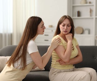 Photo of Woman apologizing to her offended friend on sofa at home
