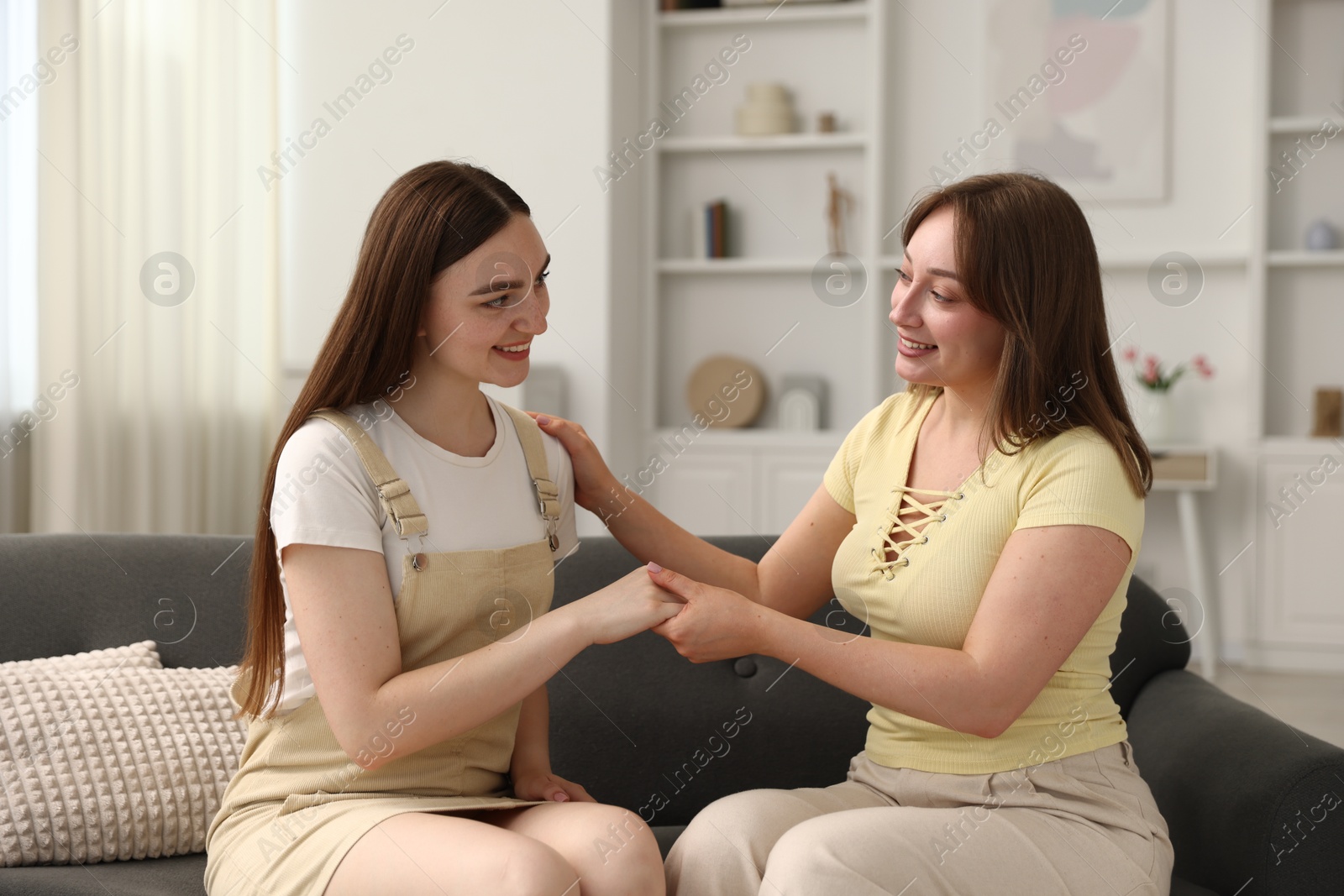Photo of Happy friends holding hands after apology on sofa at home