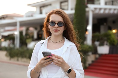 Photo of Beautiful girl with smartphone near hotel outdoors