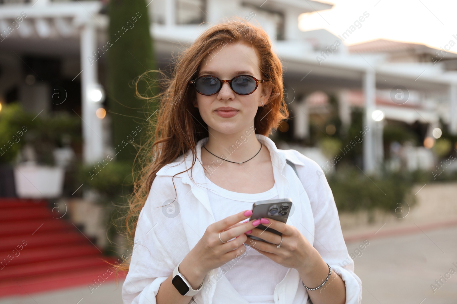 Photo of Beautiful girl with smartphone near hotel outdoors