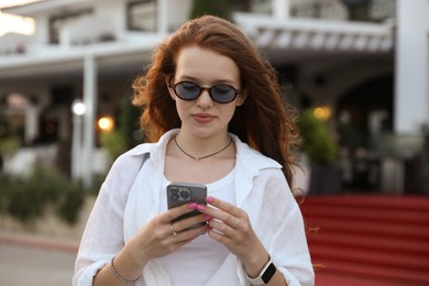 Photo of Beautiful girl with smartphone near hotel outdoors