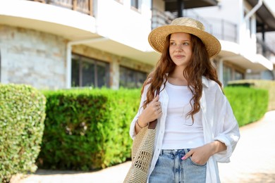 Photo of Beautiful girl in straw hat and bag near hotel outdoors, space for text