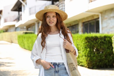 Photo of Beautiful girl in straw hat and bag near hotel outdoors