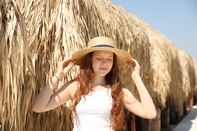 Photo of Beautiful girl in hat near straw umbrellas on beach