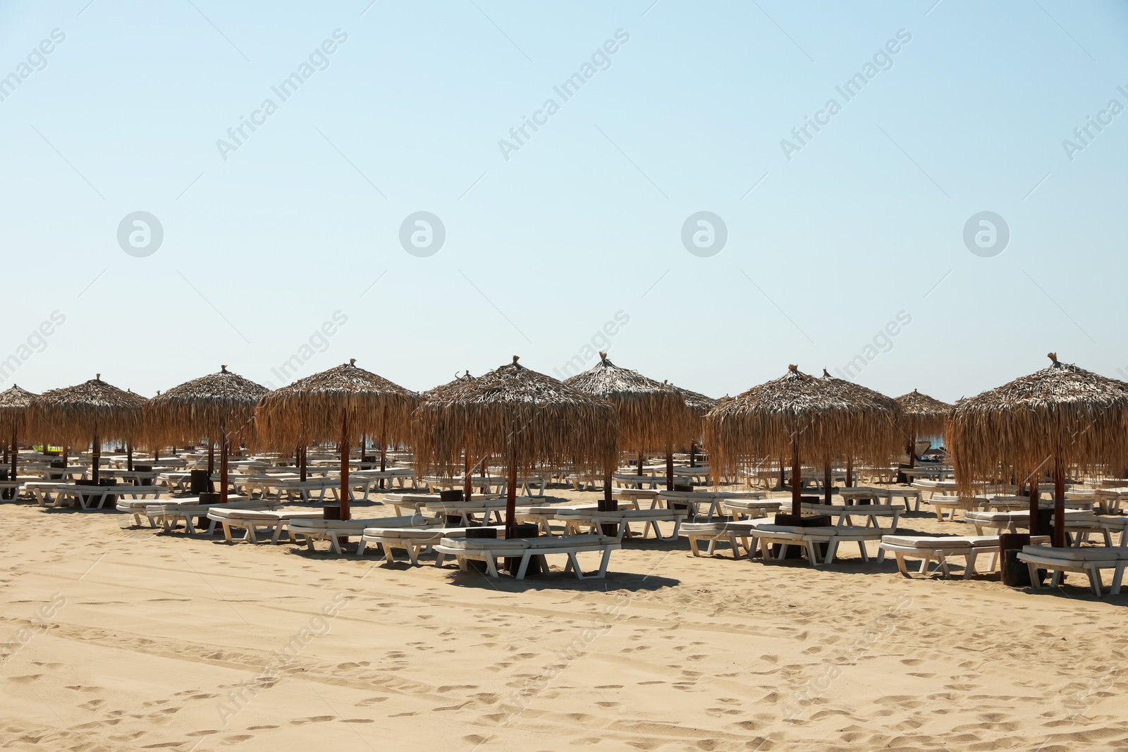 Beautiful straw umbrellas and sunbeds on sandy beach Photo of Beautiful straw umbrellas and sunbeds on sandy beach