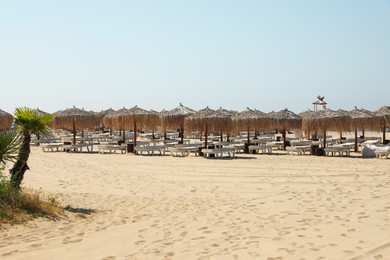 Photo of Beautiful straw umbrellas and sunbeds on sandy beach