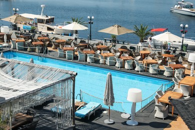 Photo of Beautiful swimming pool, sunbeds, tables, chairs and umbrellas near sea on sunny day