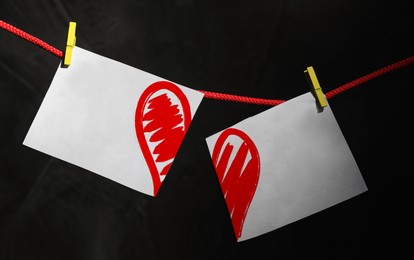Image of Betrayal. Cut in halves paper with red heart on rope against black background