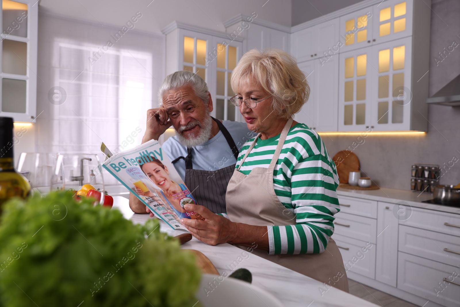 Elderly couple reading magazine together at table in kitchen Photo of Elderly couple reading magazine together at table in kitchen
