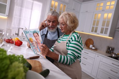 Photo of Elderly couple reading magazine together at table in kitchen