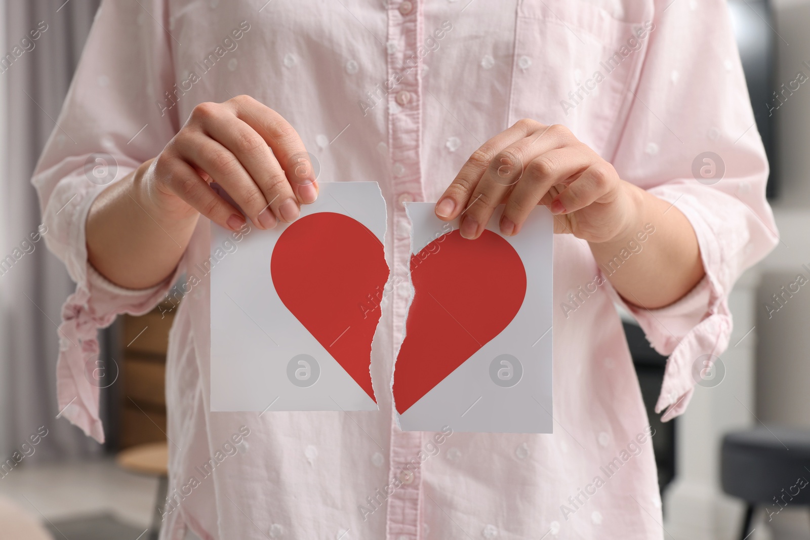 Betrayal. Woman holding torn halves of paper with red heart at home, closeup Image of Betrayal. Woman holding torn halves of paper with red heart at home, closeup