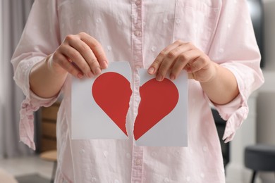 Image of Betrayal. Woman holding torn halves of paper with red heart at home, closeup