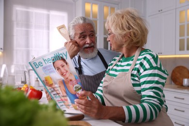 Photo of Elderly couple reading magazine together at table in kitchen