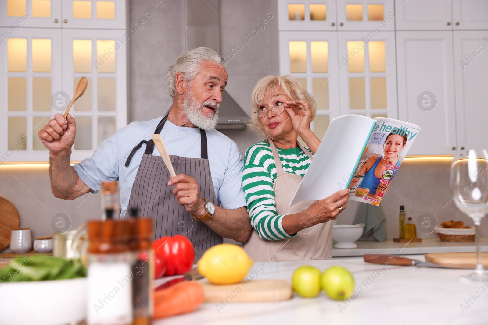Elderly couple having fun while cooking together at table in kitchen Photo of Elderly couple having fun while cooking together at table in kitchen