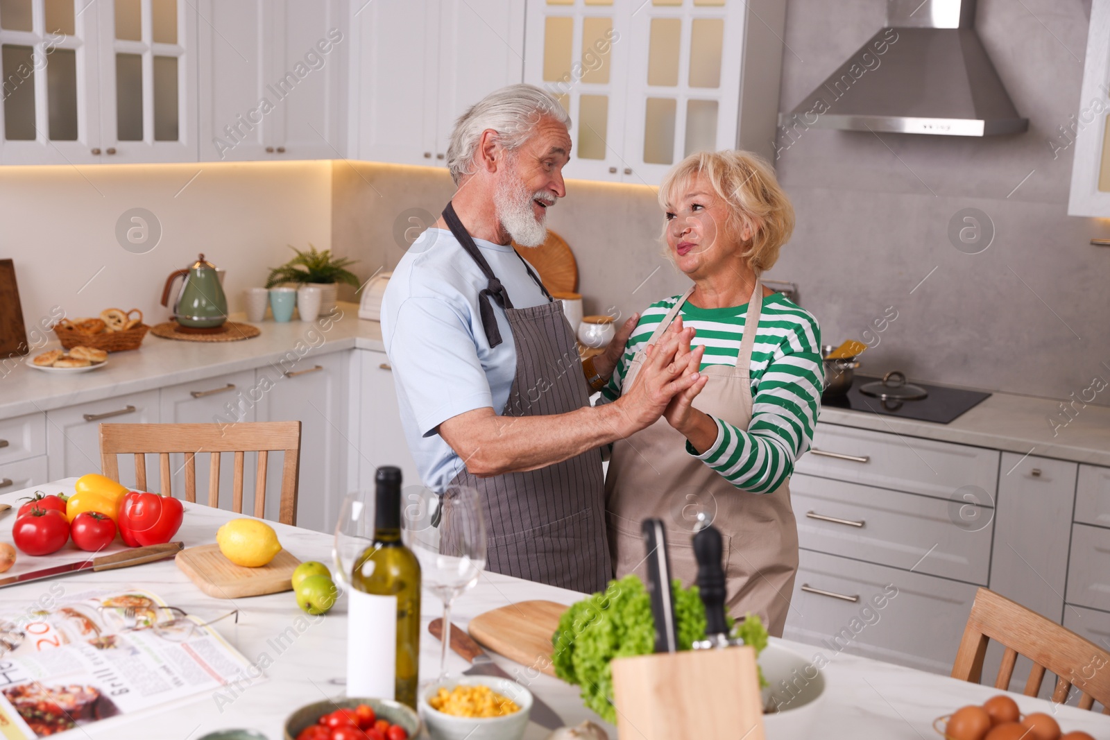 Elderly couple dancing while cooking together at table in kitchen Photo of Elderly couple dancing while cooking together at table in kitchen