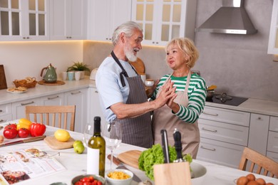 Photo of Elderly couple dancing while cooking together at table in kitchen