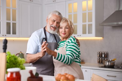 Photo of Elderly couple dancing while cooking together at table in kitchen