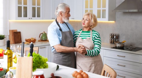Photo of Elderly couple dancing while cooking together at table in kitchen