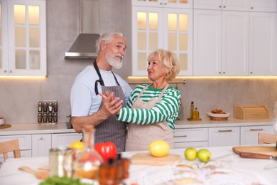 Photo of Elderly couple dancing while cooking together at table in kitchen