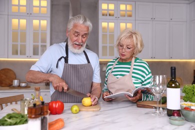 Photo of Elderly couple cooking together at marble table in kitchen